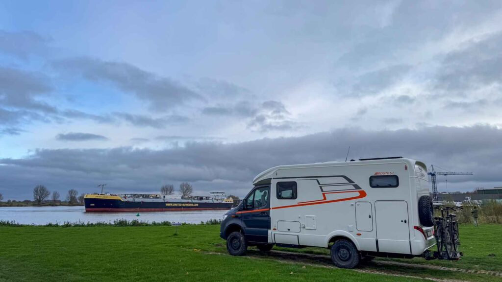 Onze camper op de camperplaats in Heusden met op de achtergrond een passerende boot op de Maas