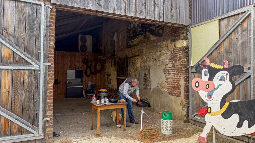 Tom staat te bakken aan de BBQ bij de ingang van de schuur op Camping De Berghemmerhof in Gulpen