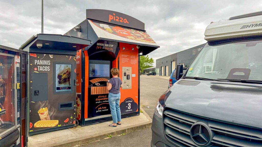 Jeannette bestelt een pizza bij de pizza-automaat onderweg naar Pau tijdens de Marokko camperreis 2026